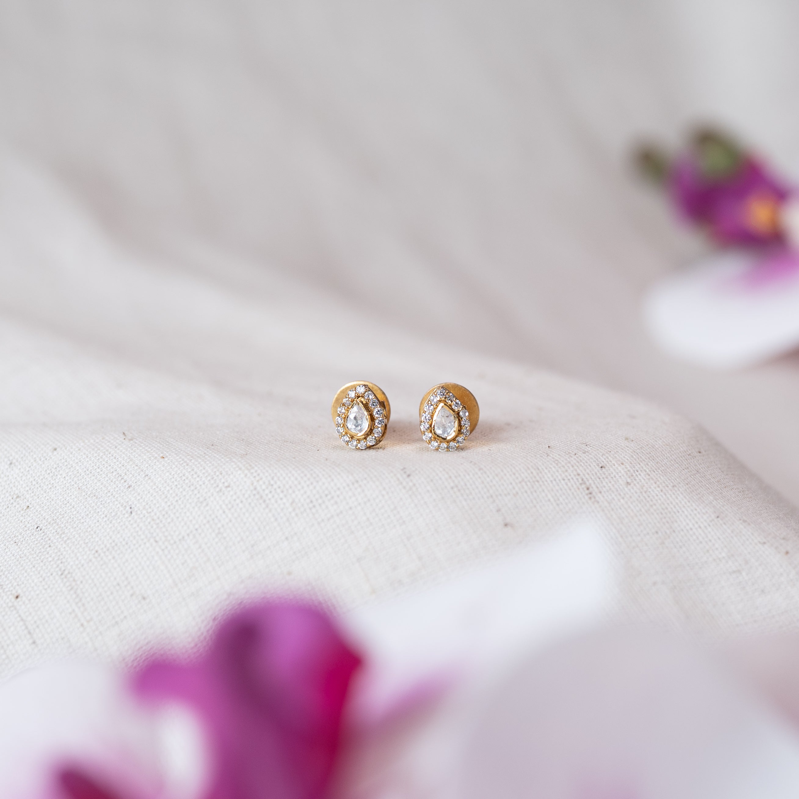 Pair of teardrop polki studs ringed with CZ, gold plated 925 silver, on linen with pink petals