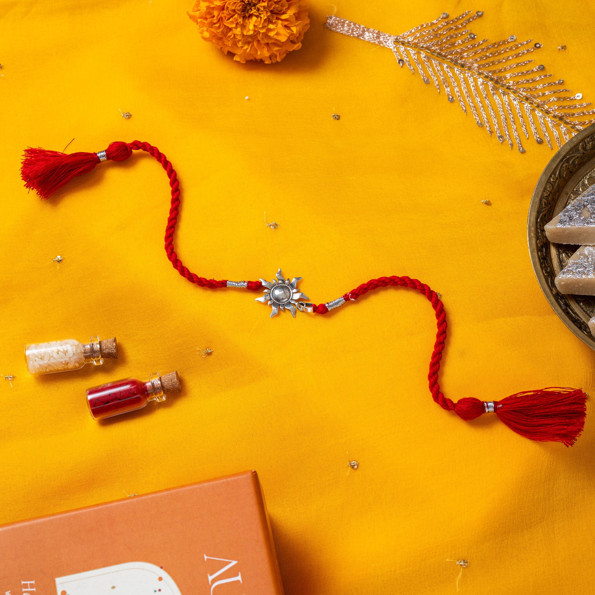 Surya sunburst with pointed rays in 925 silver on a red twisted silk rakhi cord with tassels