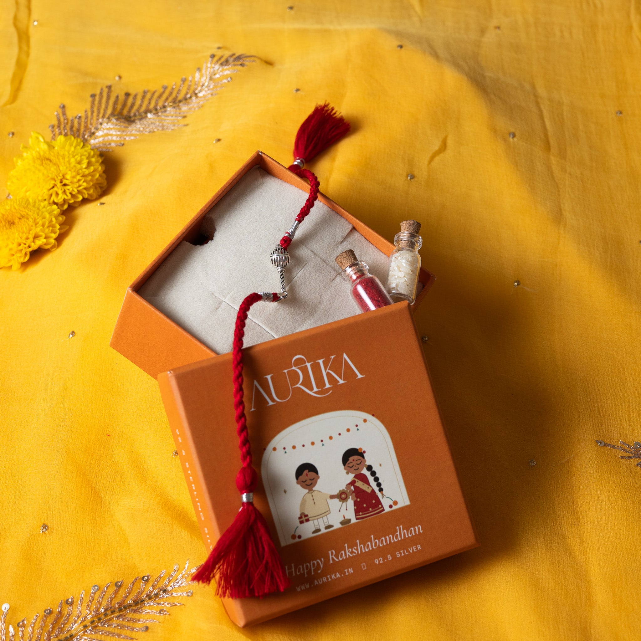 Gada mace head rakhi with its marigold cord in an open Aurika gift box on rani pink cloth