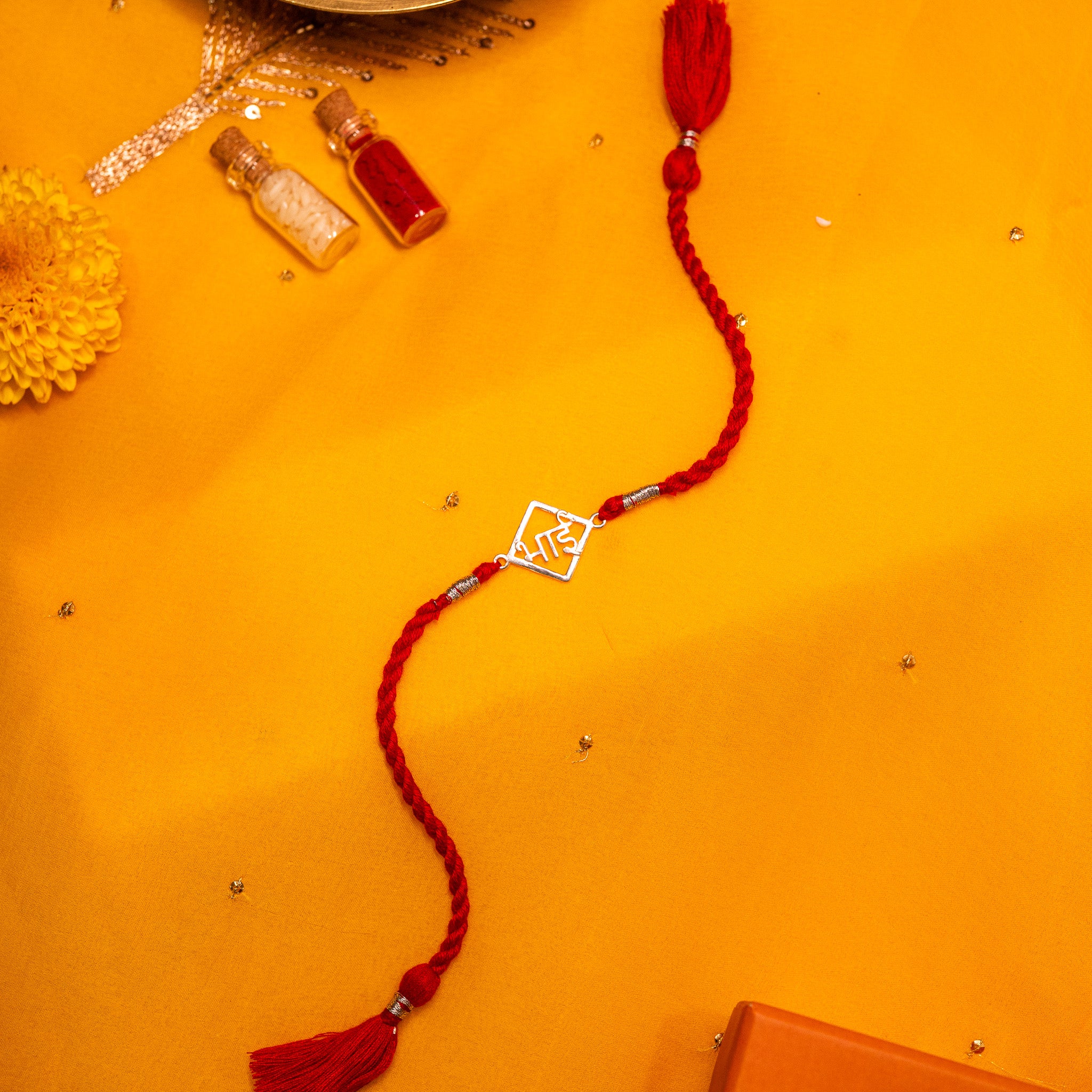 Devanagari bhai lettering in a diamond frame in 925 silver on a red twisted silk rakhi cord with tassels