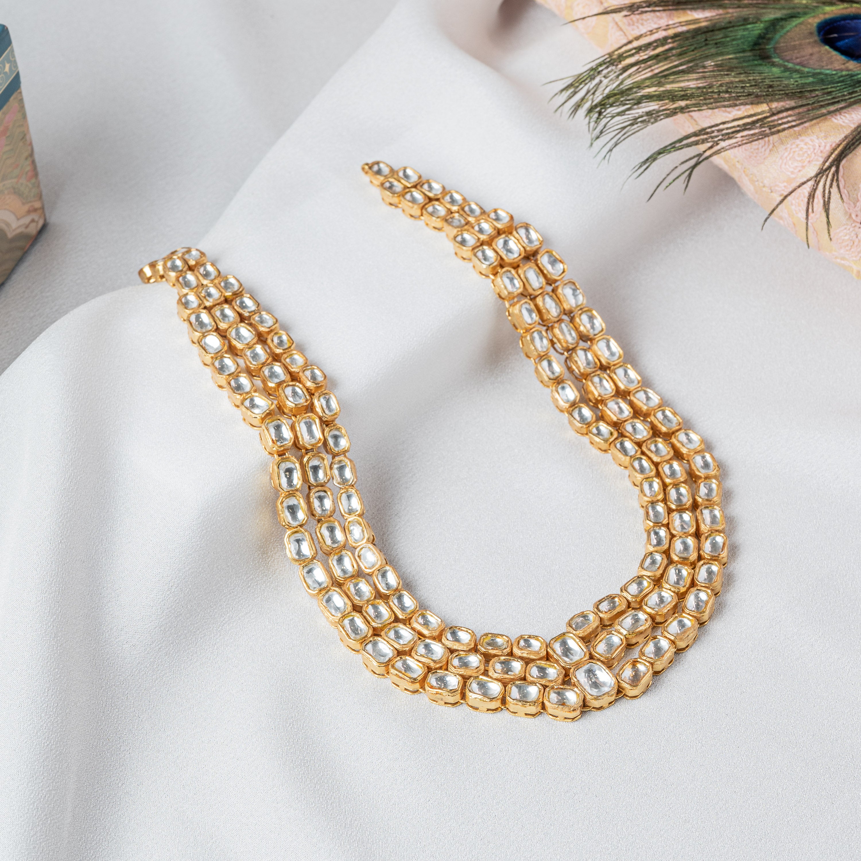 Angled view of the three graduated polki strands with a peacock feather at the side