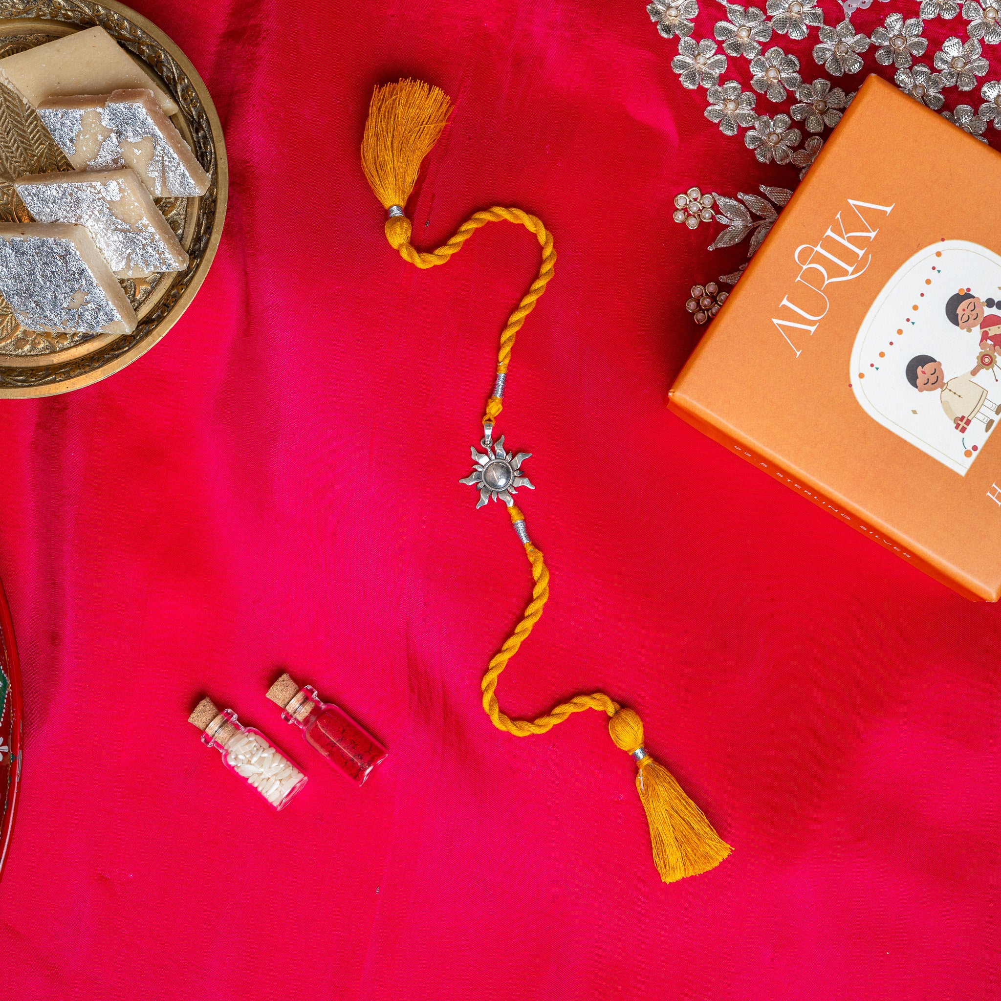 Surya sunburst rakhi in 925 silver on a marigold yellow silk cord, on rani pink cloth