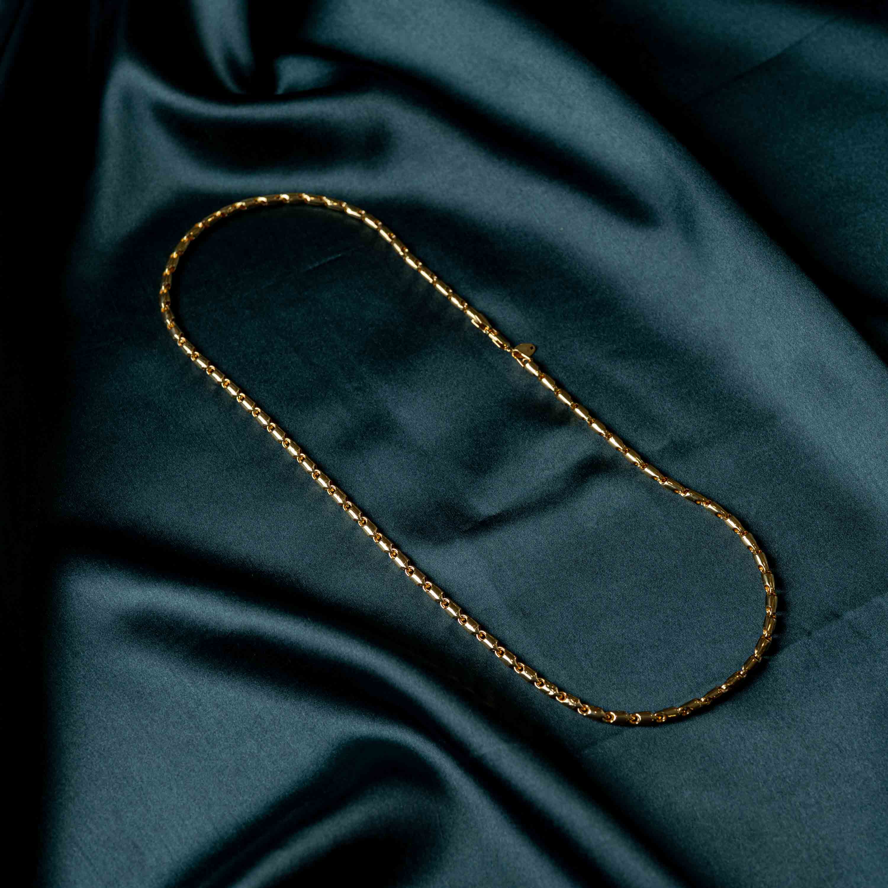 Full length of the baton link chain laid in a loop on satin, gold plated 925 silver