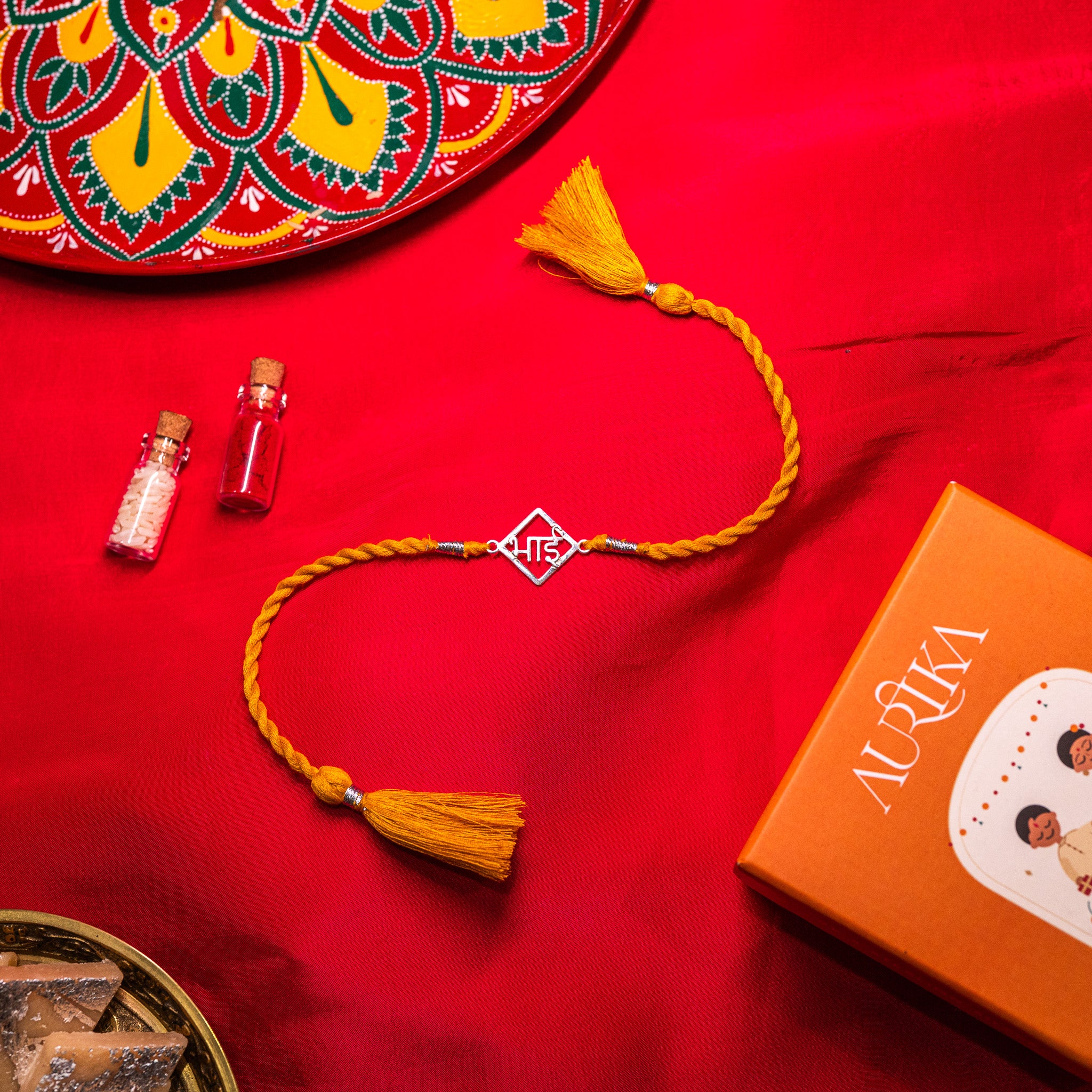 Bhai lettering rakhi in 925 silver on a marigold yellow silk cord, on rani pink cloth