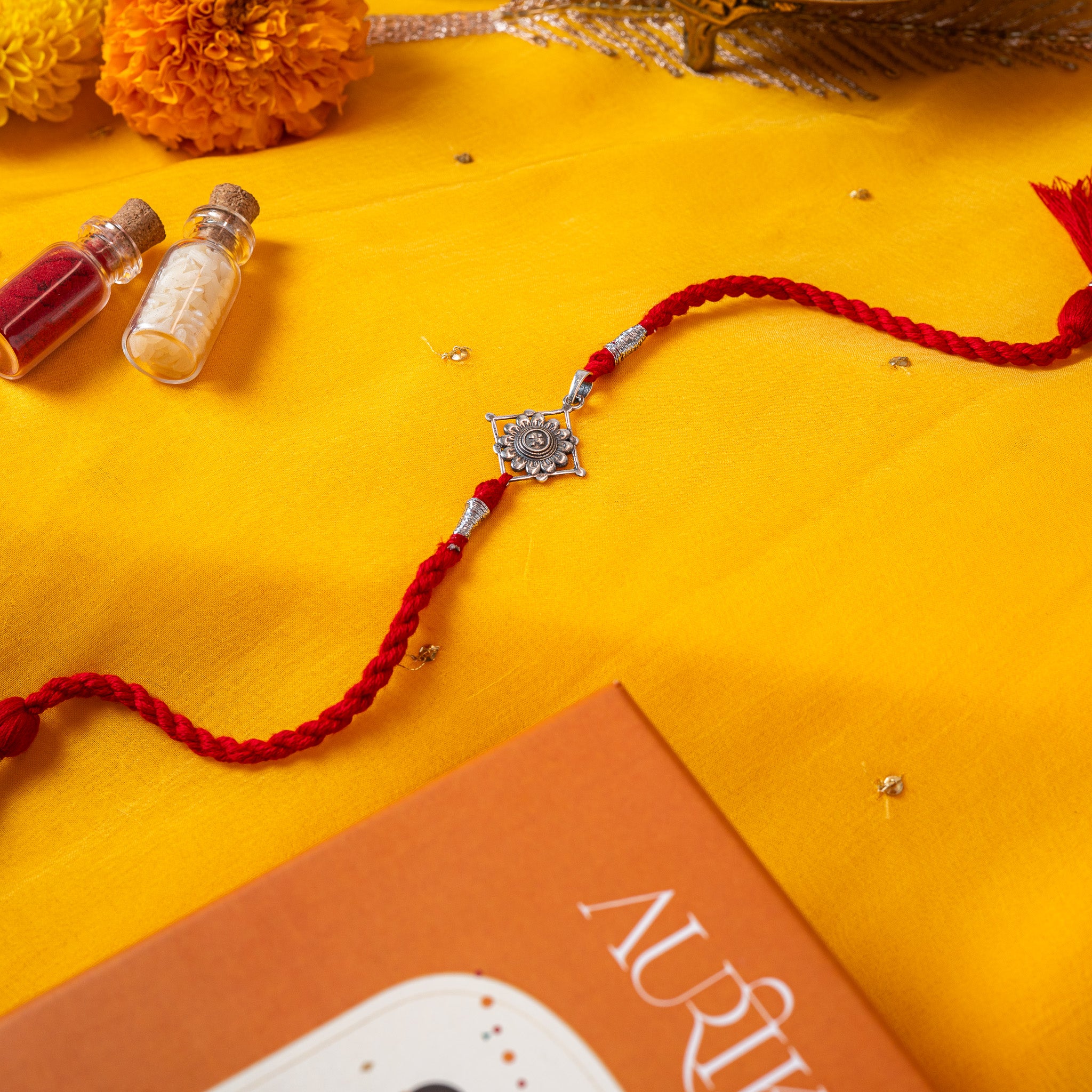 Champak flower in a beaded diamond frame in 925 silver on a red twisted silk rakhi cord with tassels