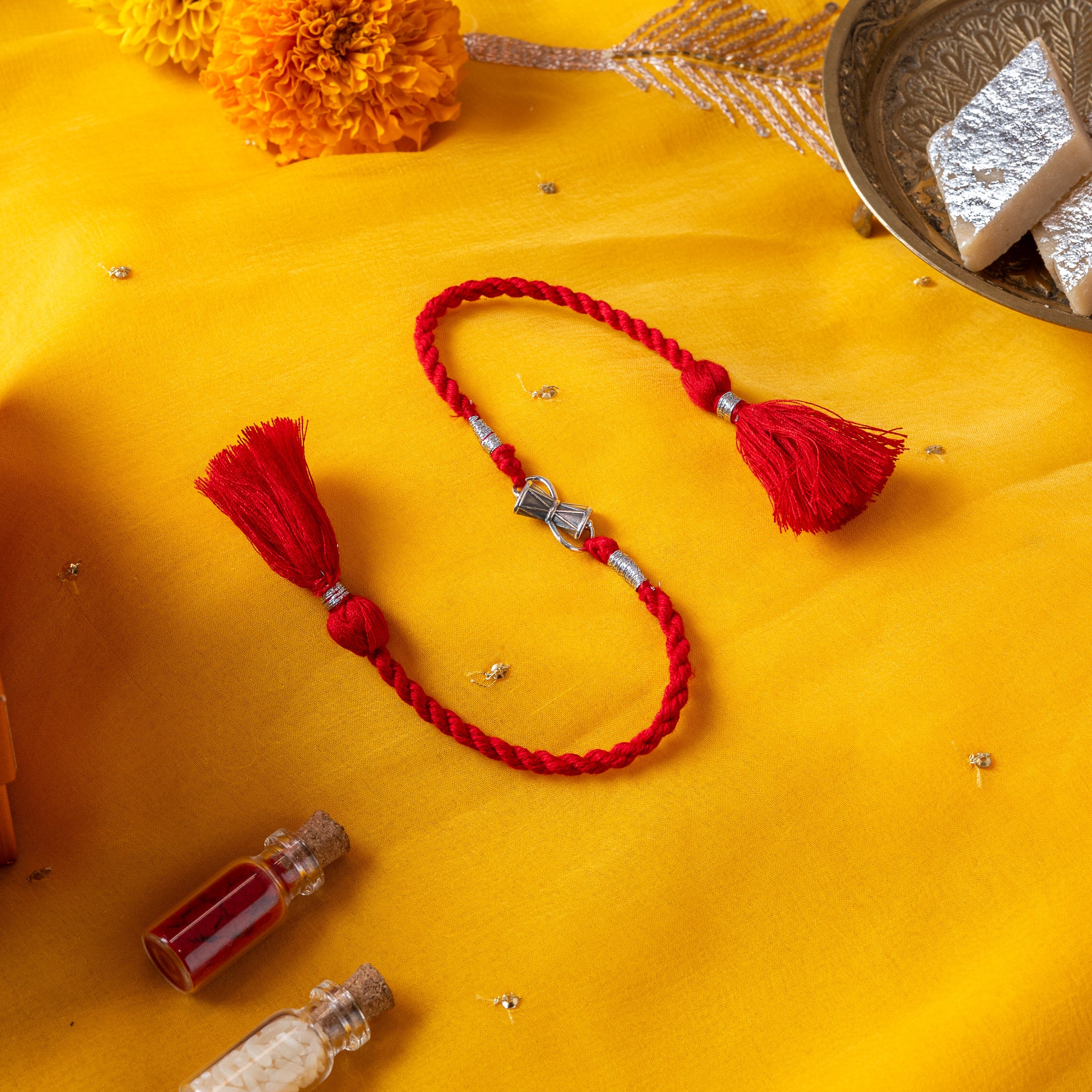 Damaru drum rakhi in 925 silver on a marigold yellow silk cord, on rani pink cloth