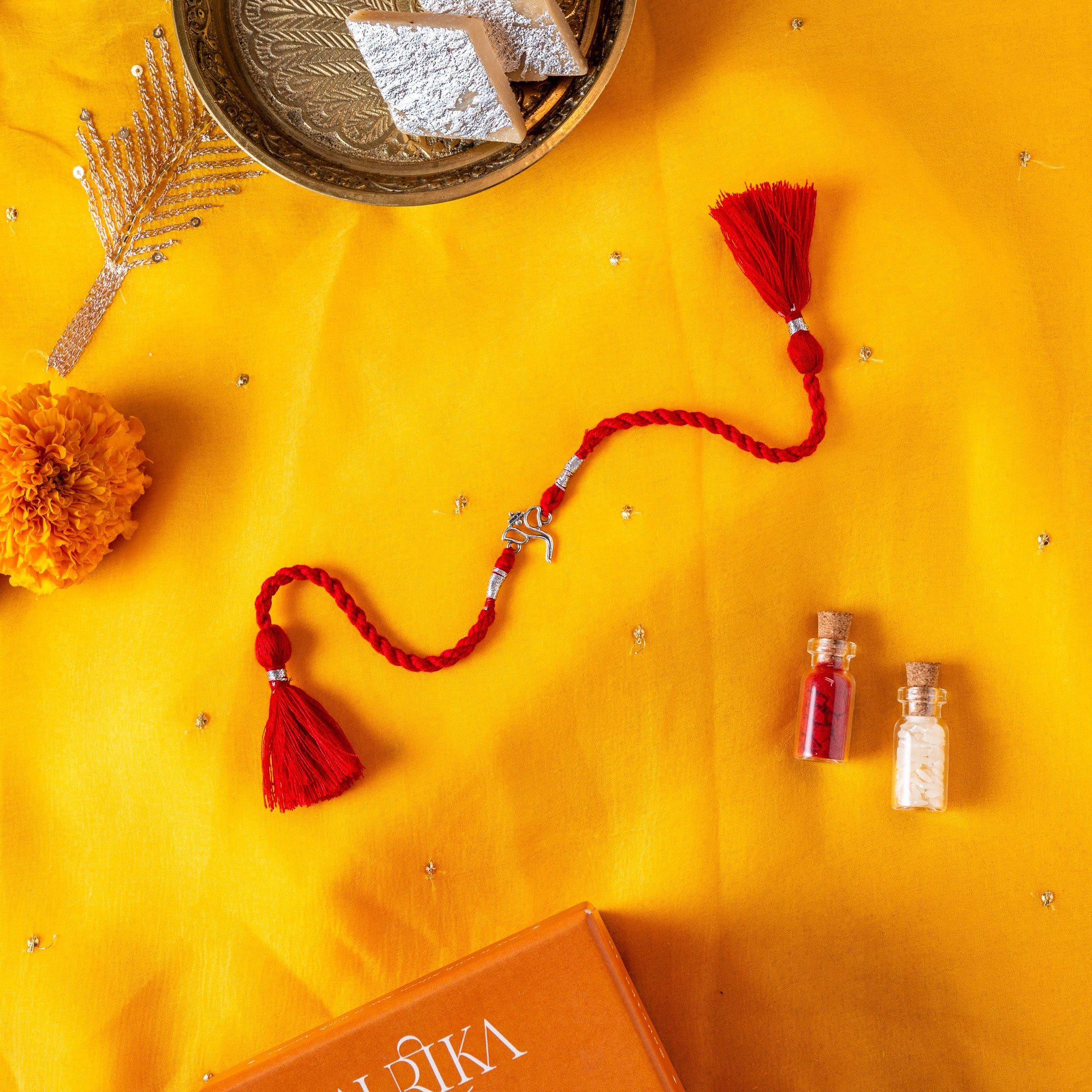 Ganesha in profile with the trunk curled down in 925 silver on a red twisted silk rakhi cord with tassels