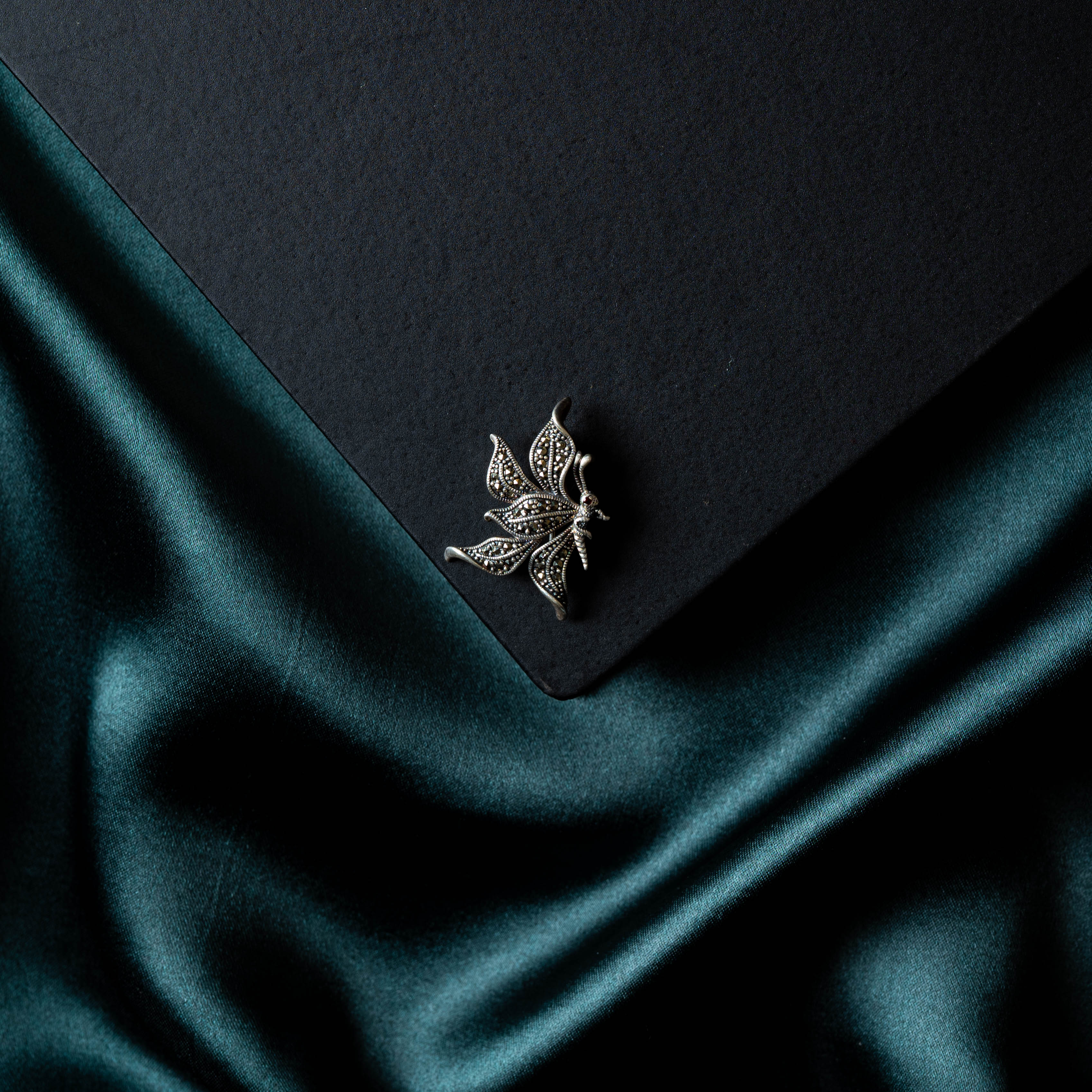 Marcasite butterfly brooch flat on a black card corner over teal satin, oxidised 925 silver