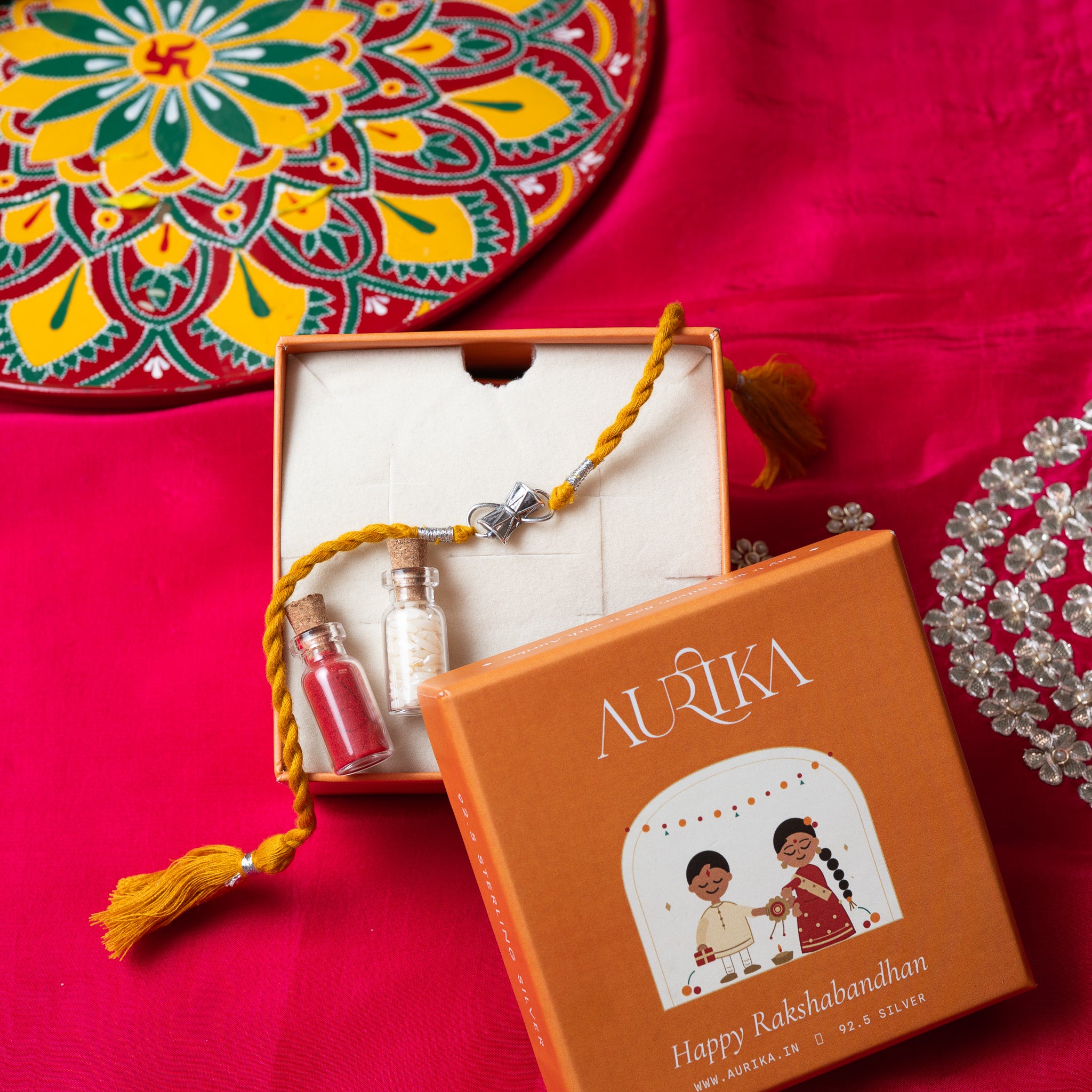 Damaru drum rakhi with its marigold cord in an open Aurika gift box on rani pink cloth