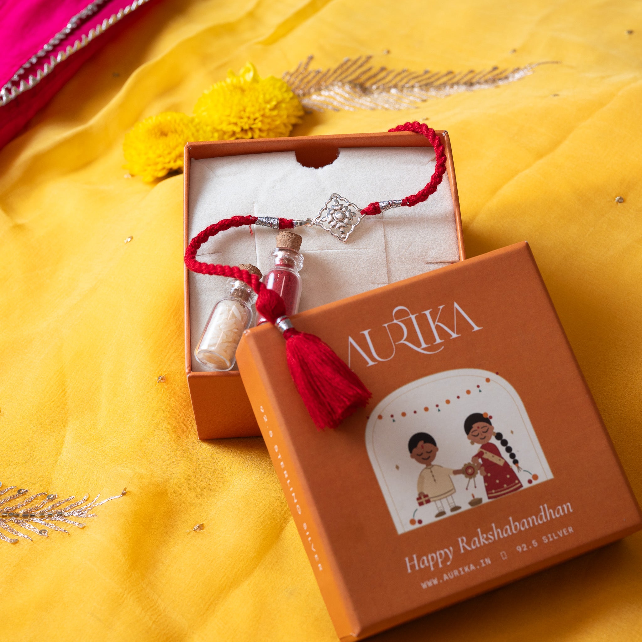 Juhi flower rakhi with its red cord in an open Aurika gift box with roli and akshat vials