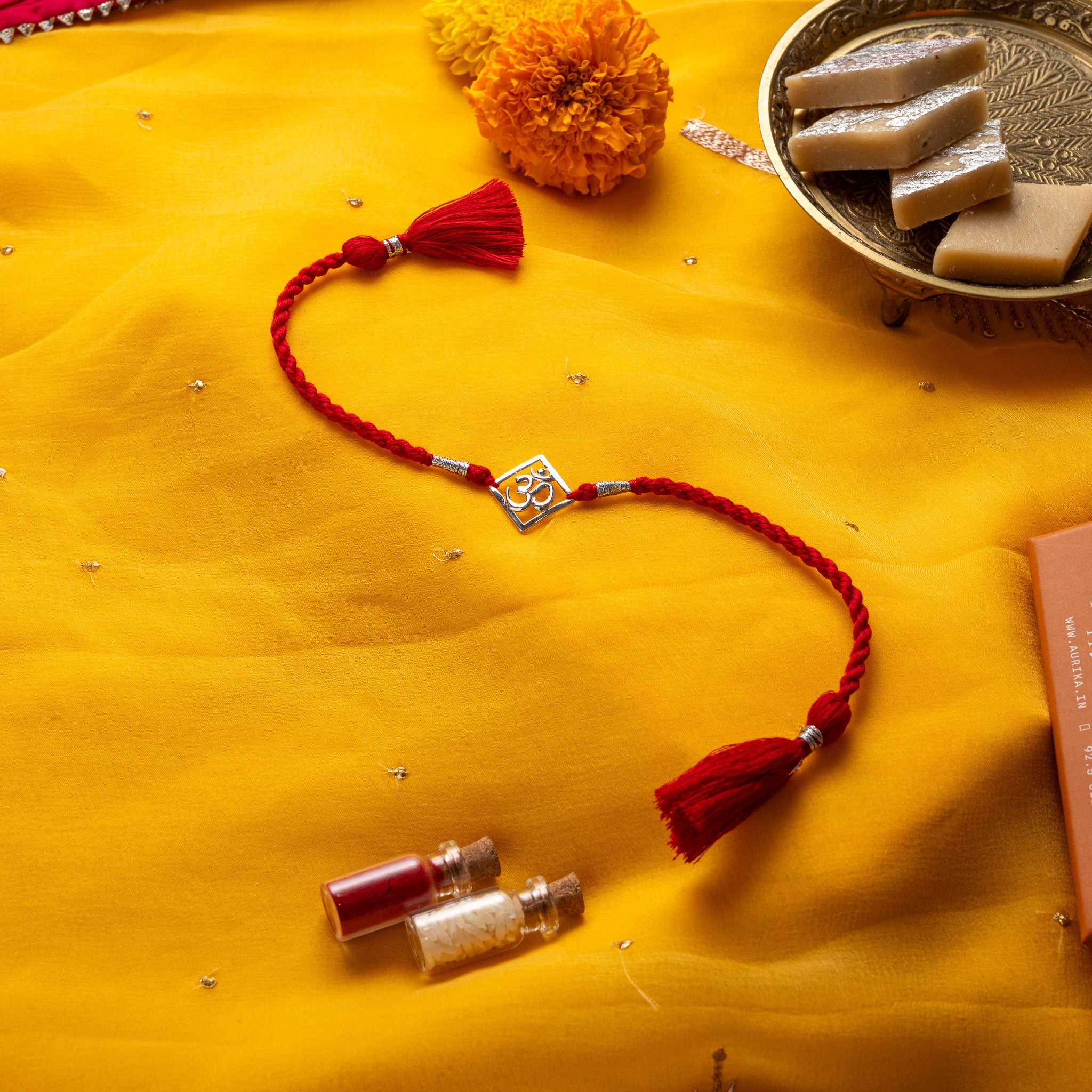 Om pierced through a square frame in 925 silver on a red twisted silk rakhi cord with tassels