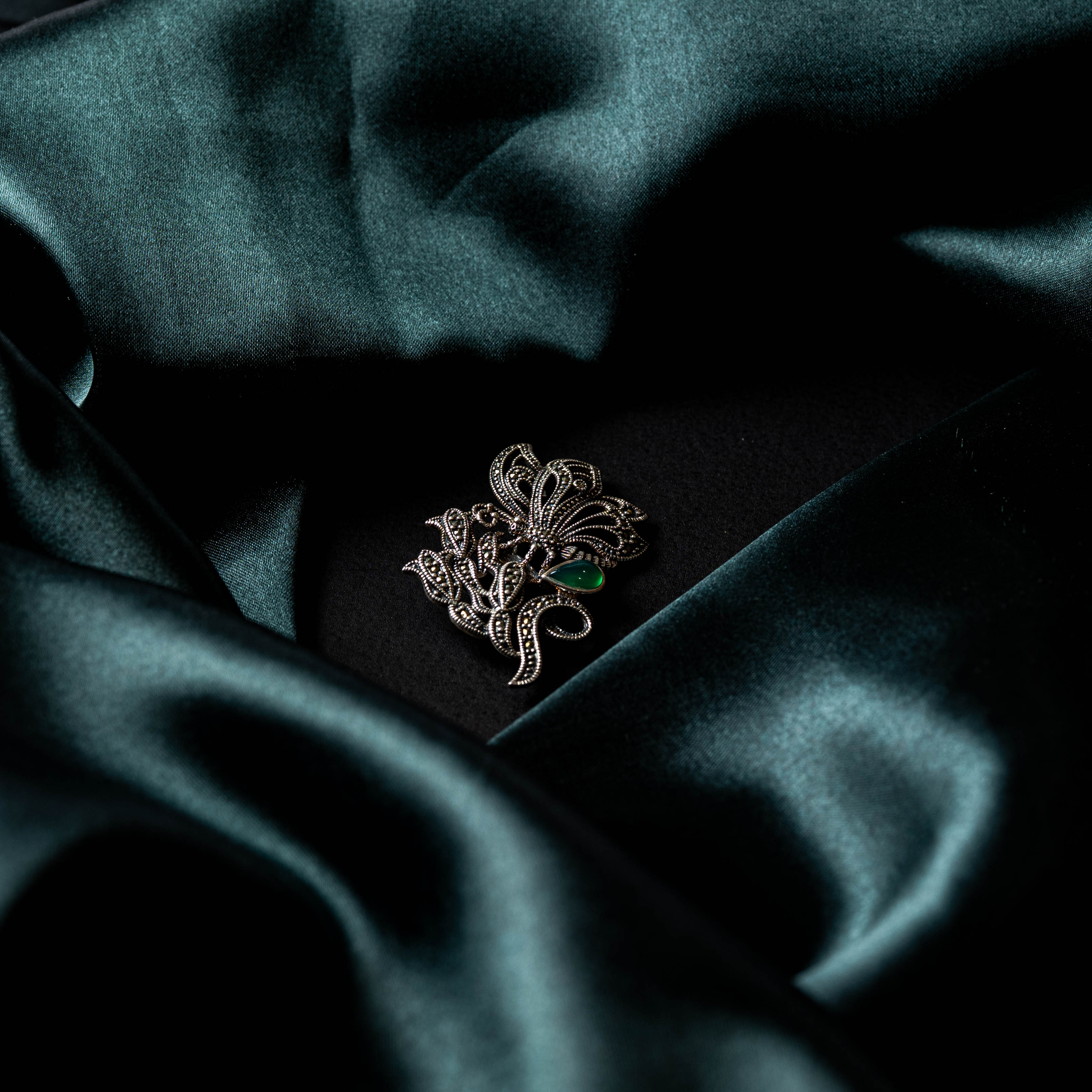 Close view of the marcasite floral scrolls and the pear cut green stone on the brooch