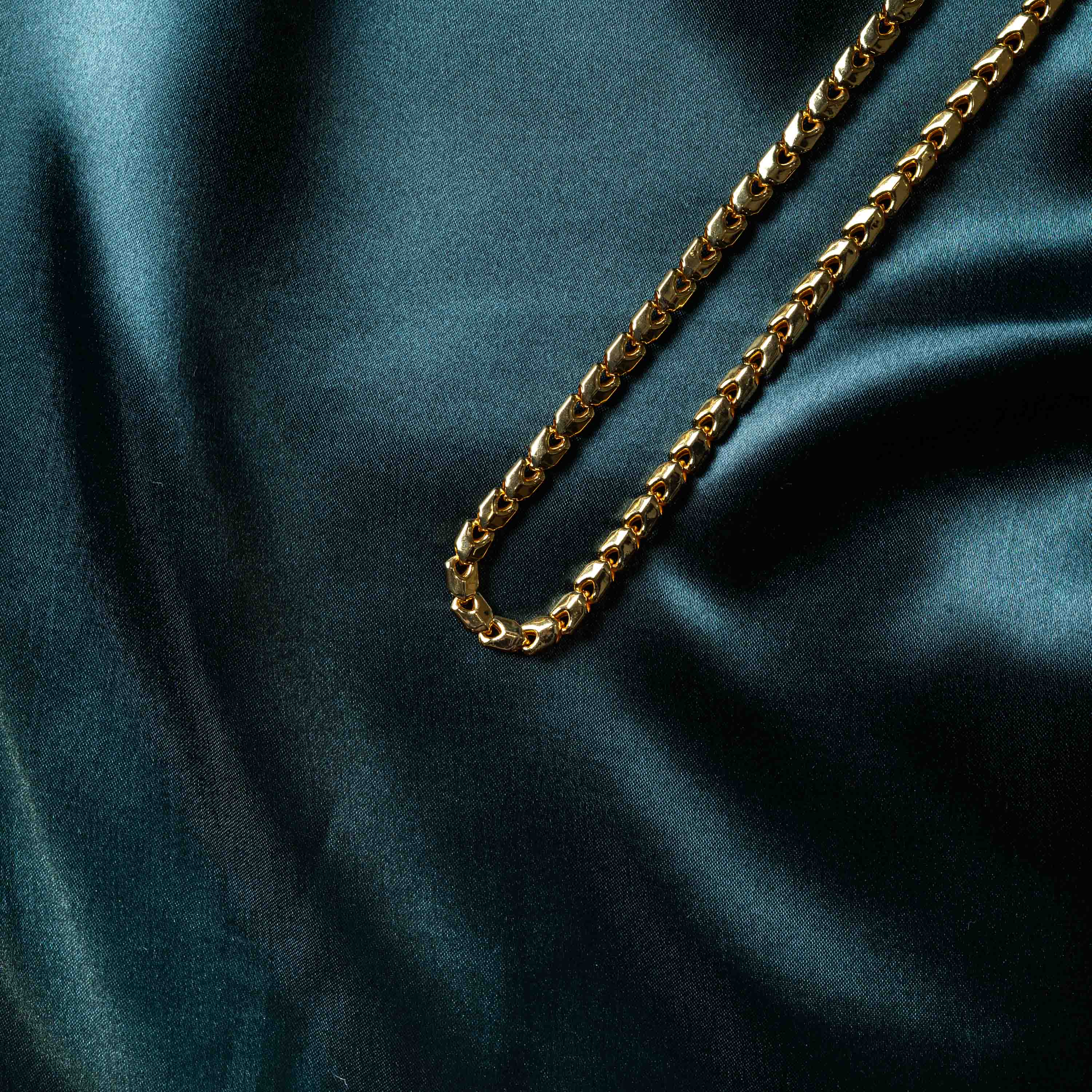 Box link chain folded at an angle, close view of the square link pattern in gold plated 925 silver