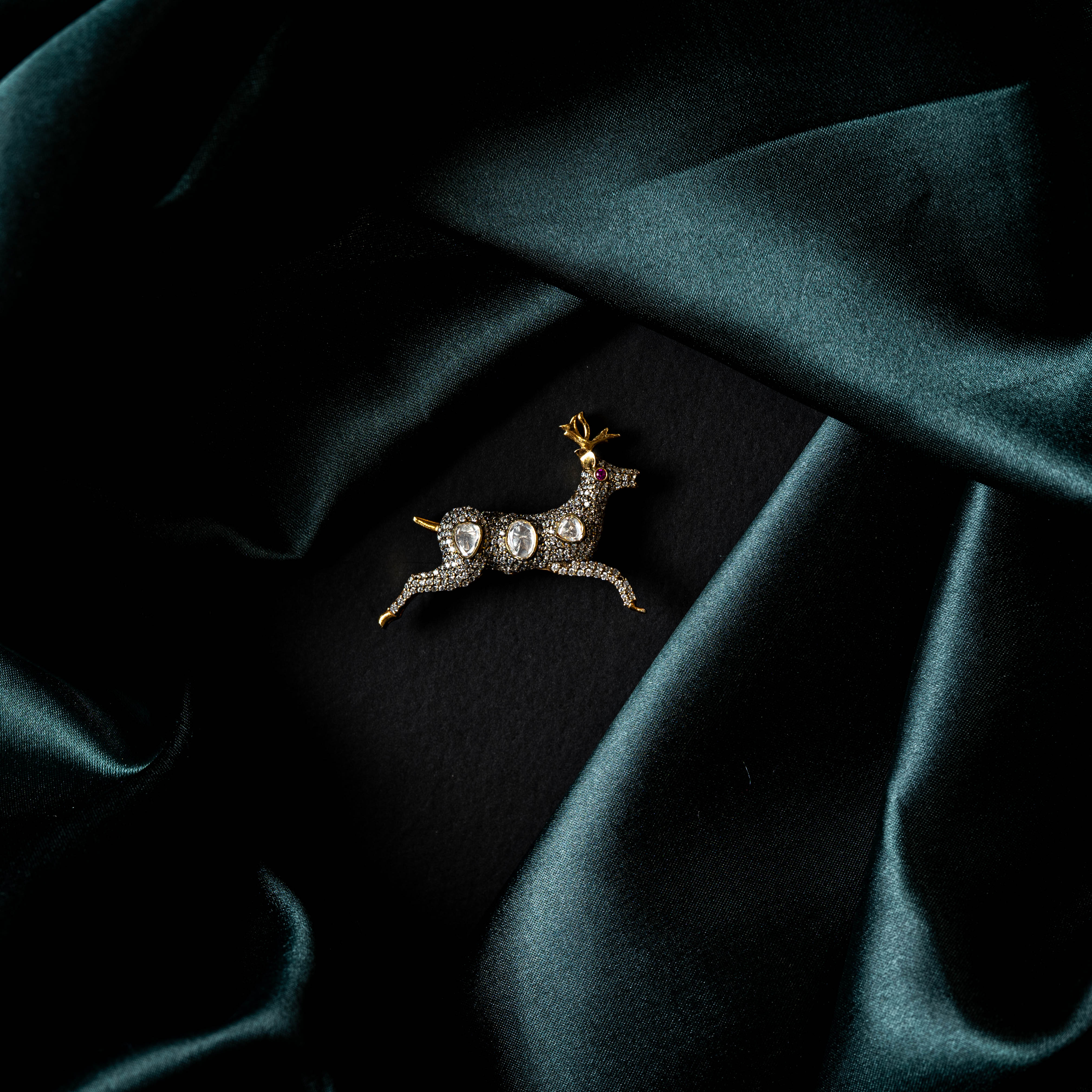 Full front view of the deer brooch on dark satin with three oval polki stones along the body