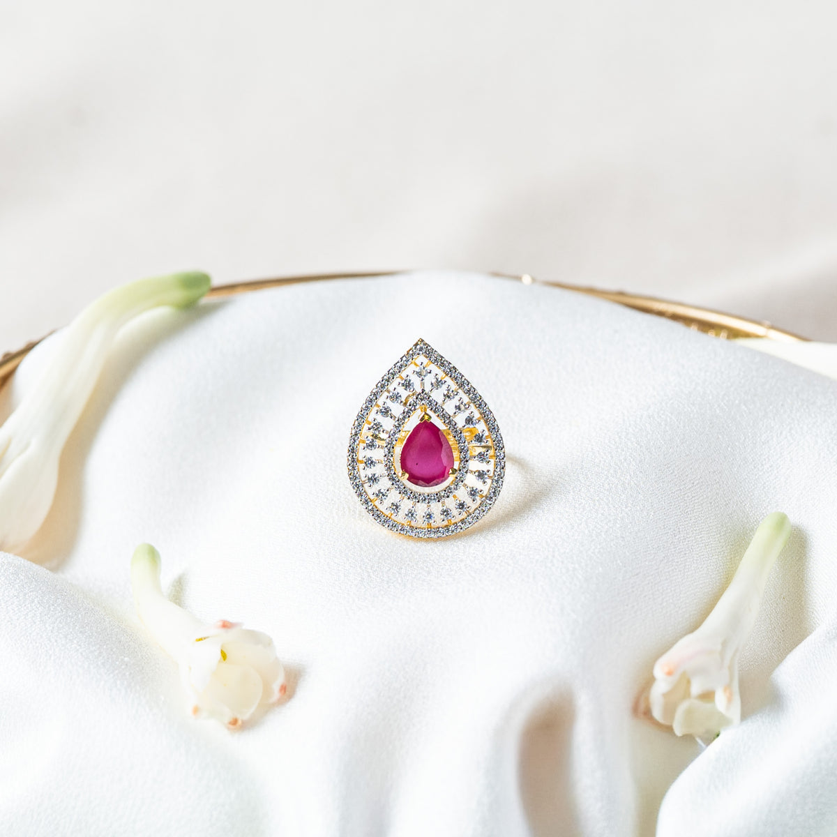 Close front view of the scalloped CZ halo around the magenta pink pear cut stone